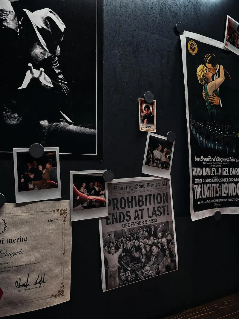 Parete con manifesti d'epoca del Proibizionismo, polaroid e attestato di mixology nella sala del Gentleman a Lecce